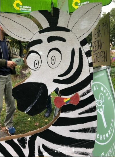 Ein Zebra aus Pappe mit einer Fliege steht vor einem Grünen Infostand