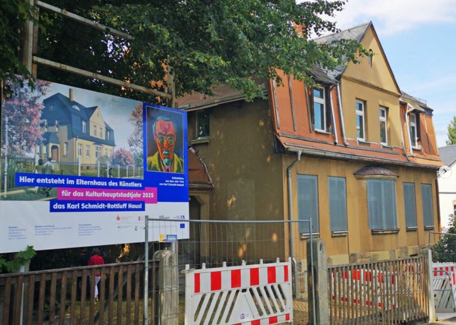 Eine Fotografie des Karl Schmidt-Rottluff Hauses. Vor dem Haus steht ein Bauschild mit angekündigten Sanierungsmaßnahmen