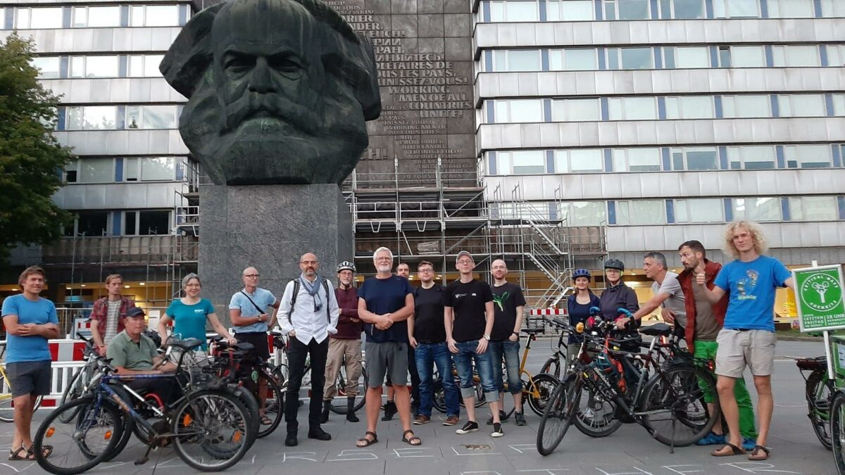 Eine große Gruppe von Leuten und Fahrrädern steht vor dem Karl-Marx-Monument in Chemnitz