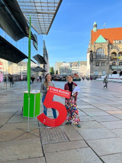 2 Frauen stehen mit einer großen roten 5 auf dem Chemnitzer Markt vor einem Grünen Infostand